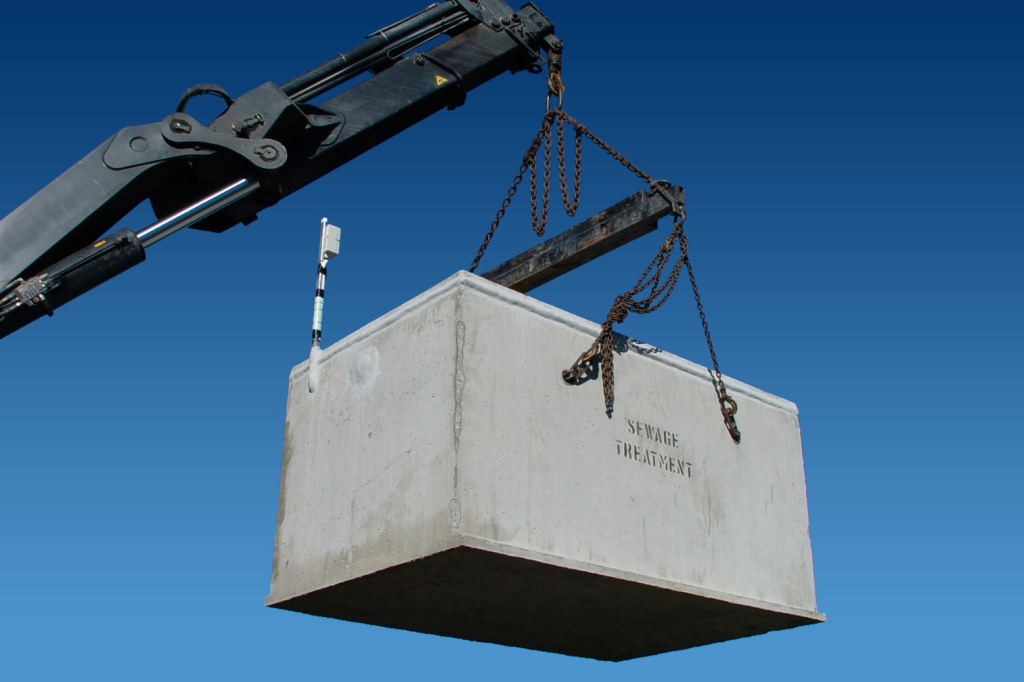 A large concrete block labeled "SEWAGE TREATMENT" is suspended in the air by chains attached to a crane against a clear blue sky background, showcasing the efficiency of modern wastewater systems.