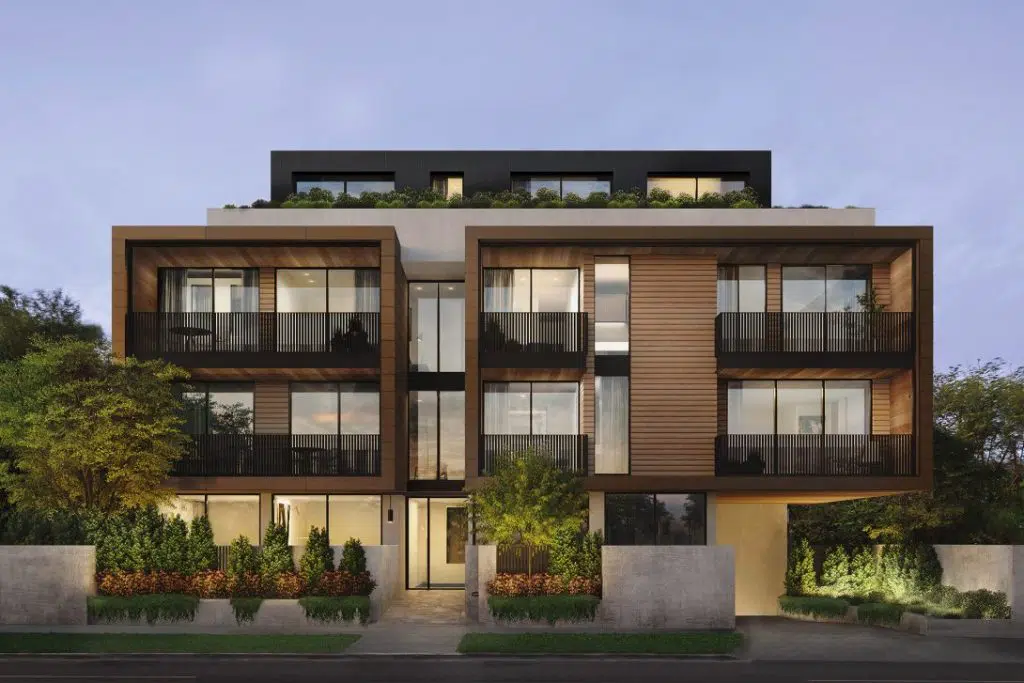 A modern, multi-story apartment building with large glass windows and wooden exterior panels. The structure features balconies for each unit and is surrounded by lush greenery and well-maintained shrubs. The development also incorporates advanced domestic wastewater systems. The sky in the background is clear, indicating evening time.